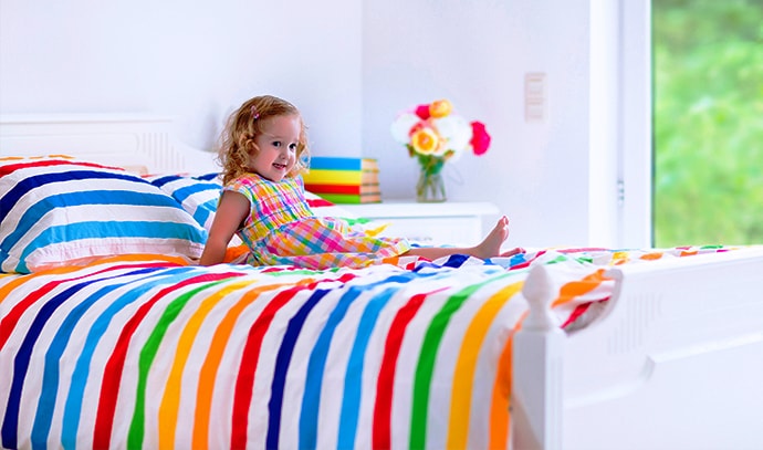 little-girl-above-white-bed-with-rainbow-striped-bedsheet