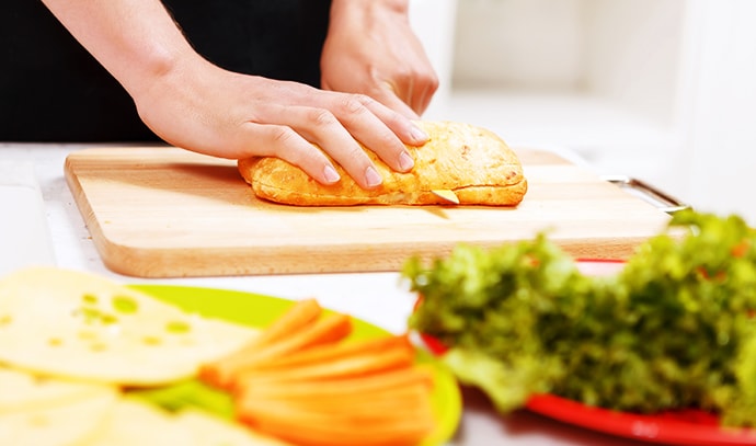 close-up-man-cutting-bread-making-sandwich-lettuce-carrots-cheese-tomato