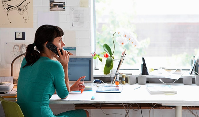 woman-talking-cellphone-home-office-table-desk