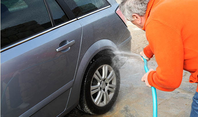 senior-man-orange-sweater-washing-car-tires-water-hose