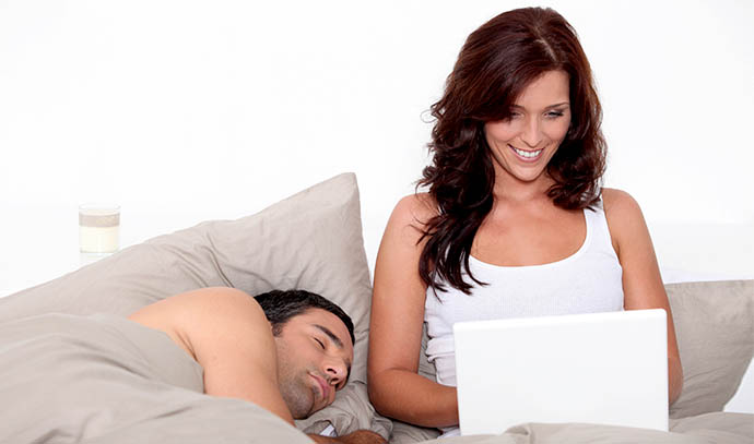 couple-sleeping-bed-woman-laptop