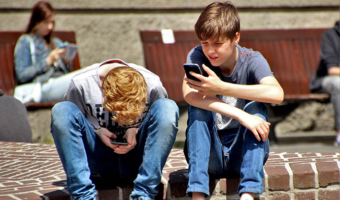 two-young-boys-teenager-using-mobile-phones-texting-browsing-outside-school